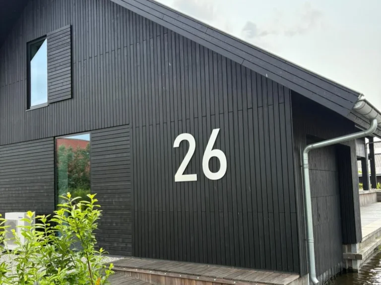 Groot RVS huisnummer 26 strak gemonteerd op een zwarte houten gevel van een moderne woning